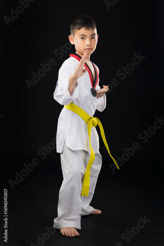 A young male taekwondo athlete wearing a white uniform and a yellow belt stands with a knife in his left hand, guarding