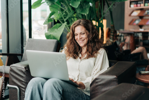 Beautiful happy cheerful woman working remotely online using a laptop while sitting in a cafe.
