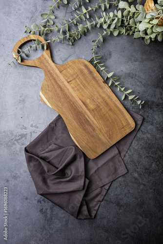 wooden cutting board on dark background with cloth and plant
