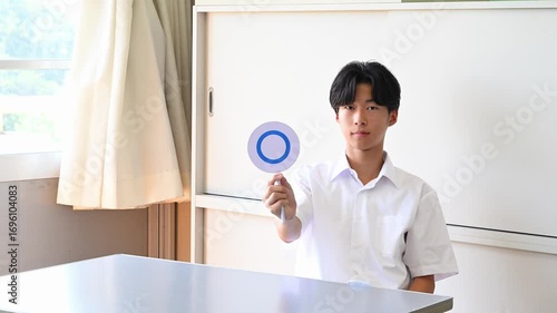 学校の教室でクイズに答える男子学生　○×で回答する学習シーン