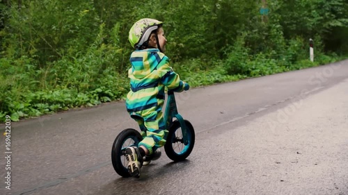 Cheerful young child enjoying balance bike ride with safety gear, developing motor skills during active family recreation time.