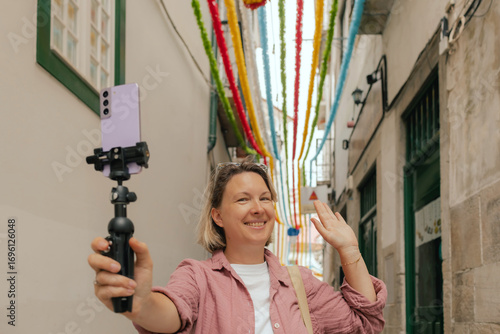 Vlogger traveler woman recording video on phone share via app travel vacation. Middle age woman influencer shooting social media stories on decorated street of Alfama district in Lisbon, Portugal