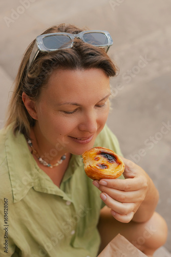 Gen Z middle age woman tries Portuguese egg tart pastry called Pastel de Nata near bakery in Lisbon. Solo tourism and travel.