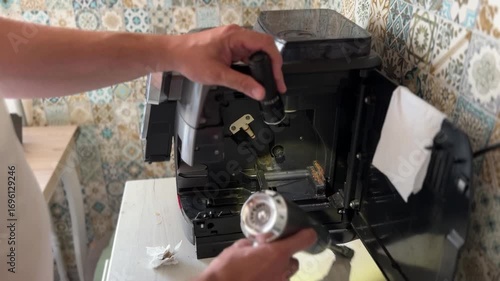 Close-up of a person's hands using a small vacuum cleaner to clean a coffee machine part on a paper towel. Focuses on home appliance maintenance