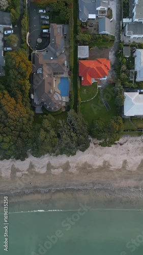Aerial view of beachfront homes in Takapuna, Auckland, New Zealand. The image shows the proximity of luxury homes to the beach and ocean. The photo highlights the desirable coastal real estate.