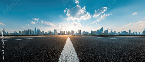 Fototapeta Naklejka Na Ścianę i Meble -  Empty asphalt road stretches into a city skyline on a bright sunny day