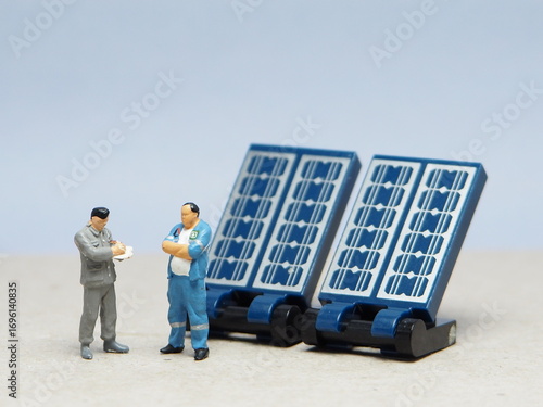 Mini toy of action figure at table with blurred background. Miniature photography concept design. Minifigure of engineer character with solar panel at outdoor.