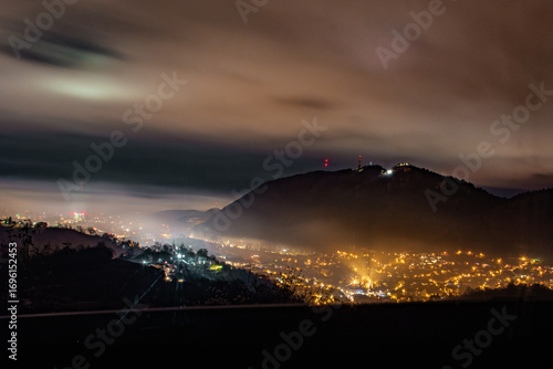 Brasov cityscape at night with glowing lights and mist from Belvedere