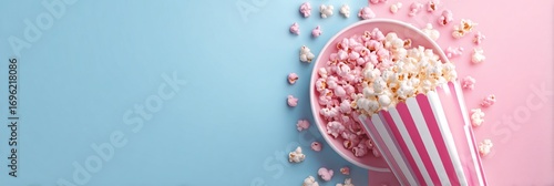 Colorful popcorn spilled out of a striped container onto a pastel blue and pink surface, creating a playful and appetizing scene perfect for snacks and movie nights.