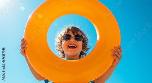 Wallpaper Mural A smiling child wearing sunglasses holds up an orange inflatable ring against a bright blue sky on a sunny day. Torontodigital.ca