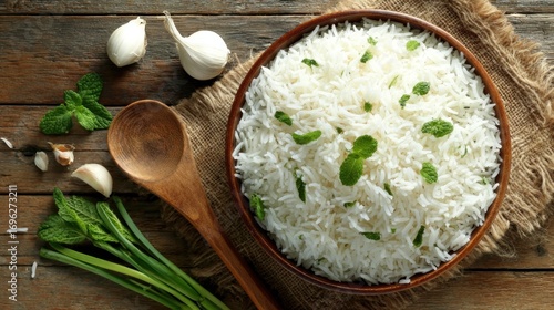 Steaming white rice, aromatic mint, garlic, and a wooden spoon lie on rustic burlap and wooden table
