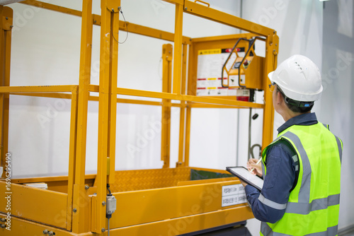 Obraz na płótnie Personal inspection of yellow lift platform by worker in safety vest and helmet