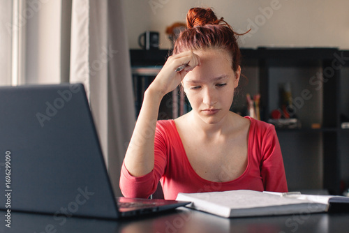 Sad and tired student girl looking on laptop and notebook