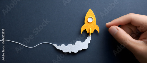 Hand launching yellow paper rocket with smoke trail on dark blue surface symbolizing startup success and innovative business ideas, creating a hopeful and inspiring atmosphere.
