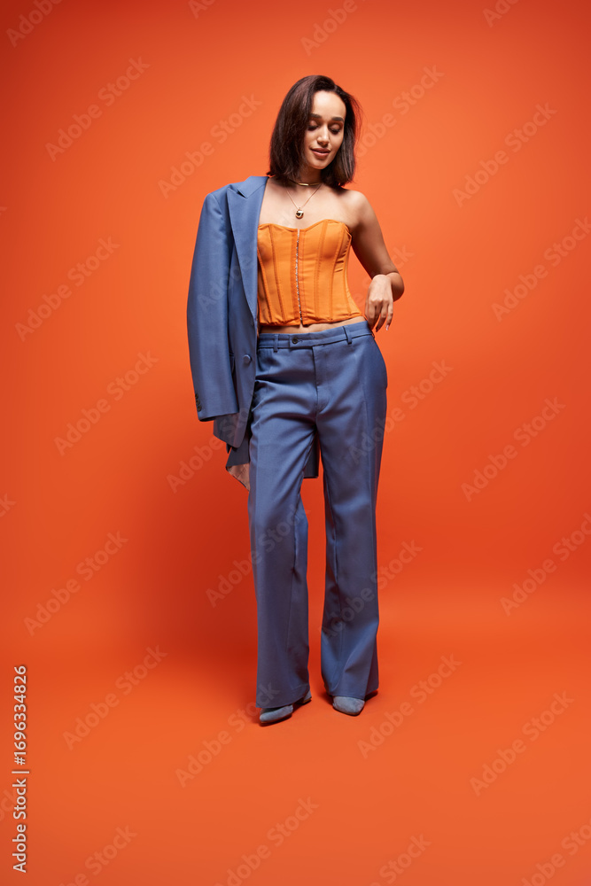 Fototapeta premium Chic young woman in blue suit and corset poses against an orange background