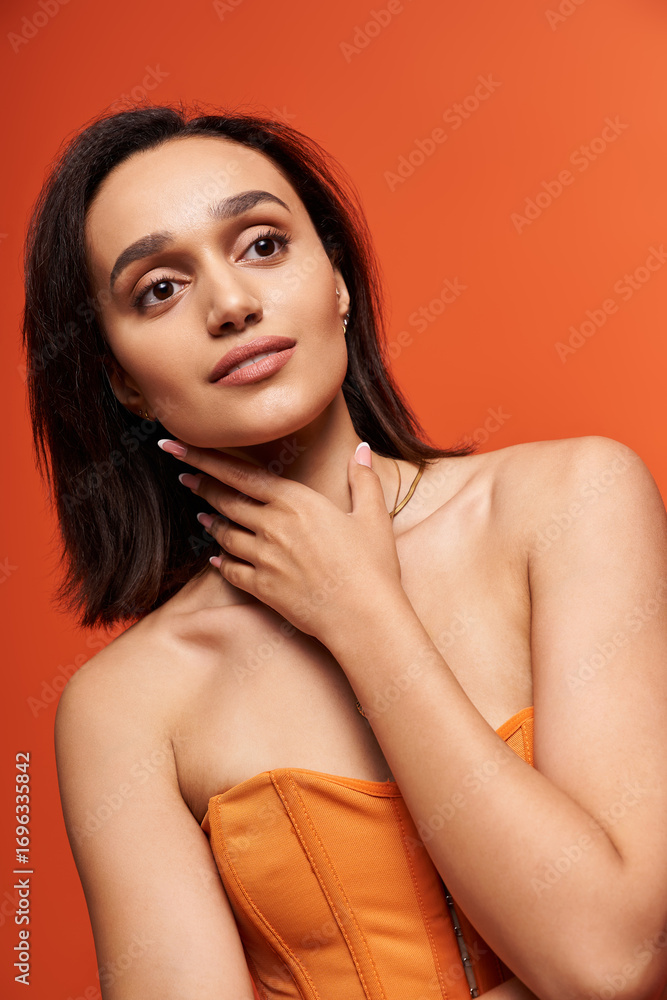 Naklejka premium Brunette in orange corset poses elegantly in a chic studio