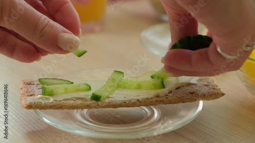 Close up of woman hand pouring sliced cucumber on crispy bread with cheese. The importance of healthy breakfast, snack and ease of meal preparation.