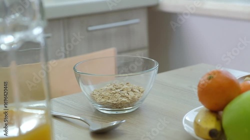 Close-up of a person's hands steams oatmeal with boiling water into a glass bowl with other fruits nearby. Represents healthy eating and morning routine