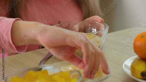 close-up of a girls hands preparing a bowl of cereal with fresh fruit, emphasizing healthy eating, breakfast, and a morning routine