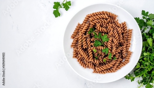 Spiral whole wheat pasta on white plate with fresh parsley