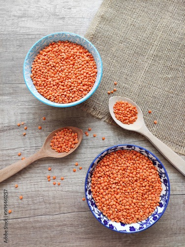 Dried small red lentils in a decorative plate and wooden spoons on a wooden background