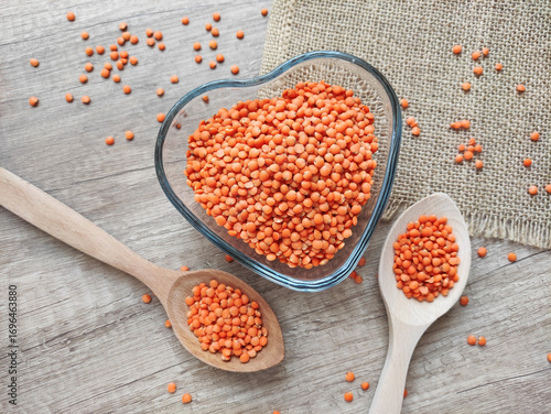 Dried small red lentils in a decorative plate and wooden spoons on a wooden background