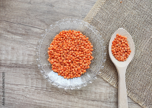 Dried small red lentils in a decorative plate and wooden spoons on a wooden background