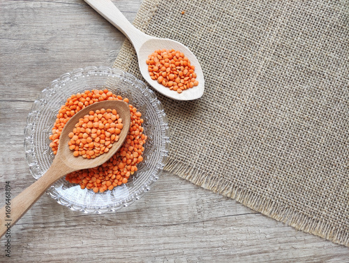 Dried small red lentils in a decorative plate and wooden spoons on a wooden background