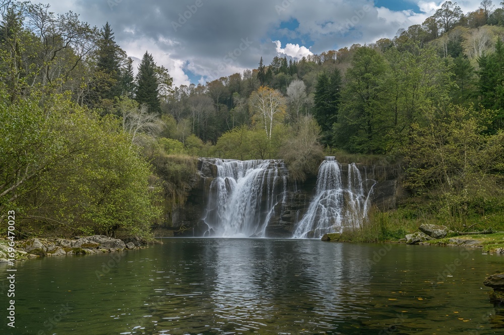 Fototapeta premium Scenic countryside featuring a cascading waterfall amidst lush greenery