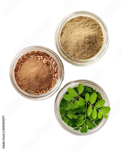 Three clear glass jars; top-down view.  A light tan powder, a dark brown powder, and fresh green leaves are visible within.  Natural health supplements or ingredients