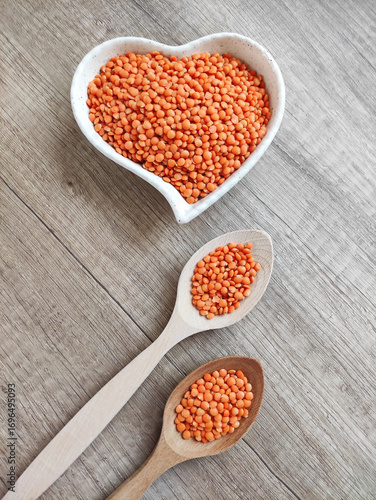 Dried small red lentils in a decorative plate and wooden spoons on a wooden background