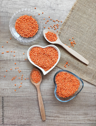 Dried small red lentils in a decorative plate and wooden spoons on a wooden background
