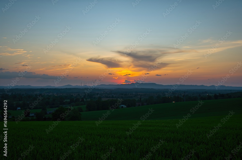 Fototapeta premium Silhouetted hills and lush meadows under a sunset sky