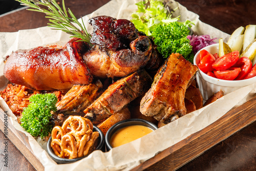 Canvas Print Rustic meat platter with ribs, pulled pork, ham hock, sauces, pickles, pretzels, and greens on parchment over wood