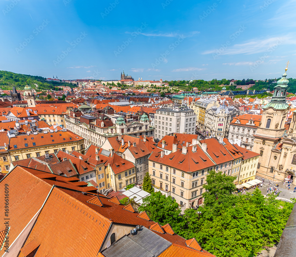 Obraz premium An aerial view across the rooftops towards the distant castle complex from the City Hall tower in the old town square in central Prague in springtime