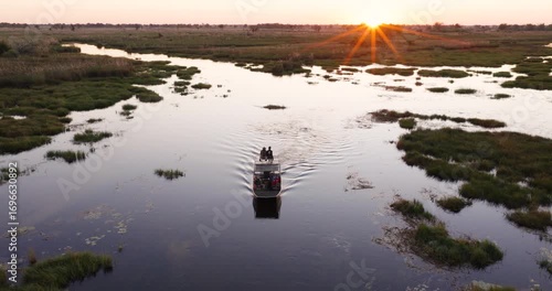 High aerial. Tourists on a sightseeing boat on a river in the Okavango Delta at sunset