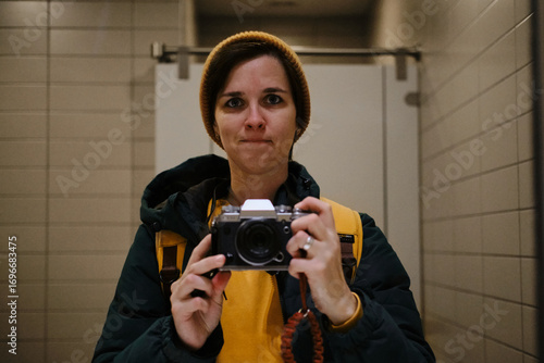 Valokuva Woman in yellow beanie and jacket taking a mirror selfie with a retro camera in