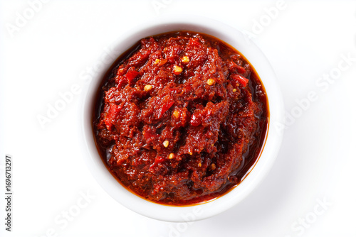 Spicy red chili paste in a white bowl with visible pepper flakes. Fiery condiment isolated on white background, highlighting rich texture and bold flavor.
