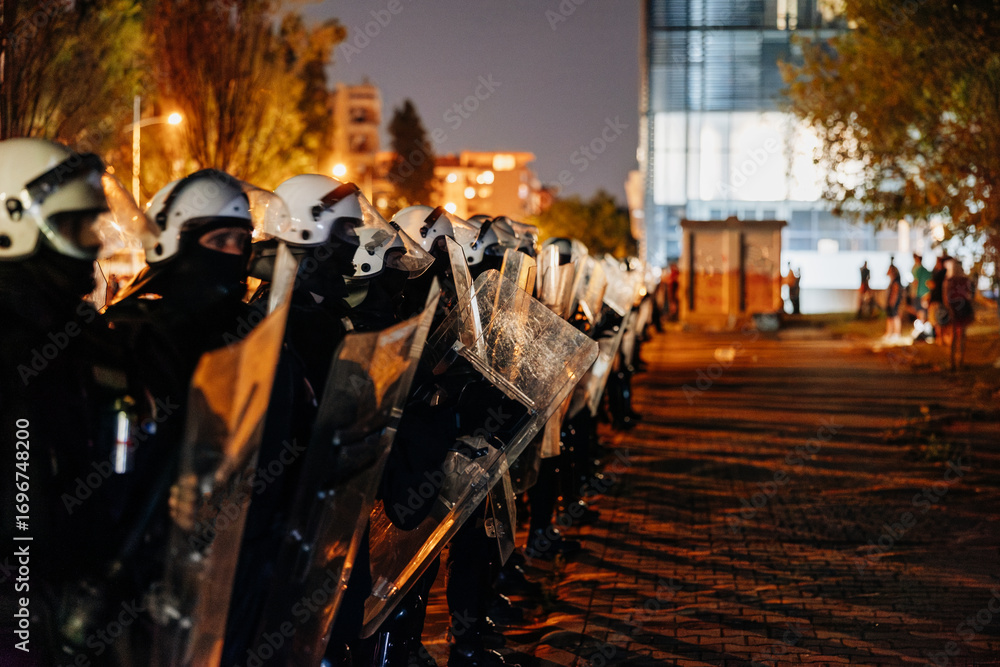 Naklejka premium Law enforcement officers in riot gear standing firm during nighttime protest in urban area