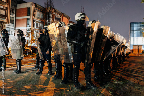 Riot police stand ready during a nighttime protest in an urban area amid tensions and unrest