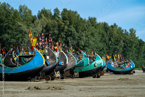Colorful Fishing Boats Lined Up on Sandy Shore with Flags. Colorful Wooden Fishing Boat On a Cox's Bazar Sea Beach, Bangladesh With Blue Sky Background. 