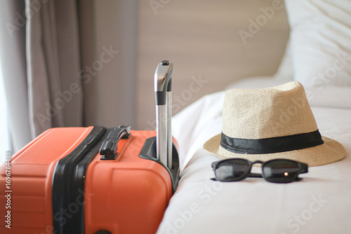 Luggage and beach hat of a couple on bed in modern hotel room with windows, curtains. Travel, relaxation, journey, trip and vacation concepts. Closeup