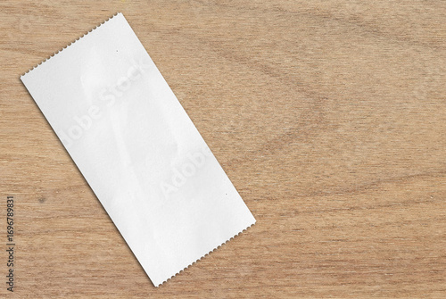 Cash receipt paper on oak wood table. blank purchase bill invoice or supermarket shopping retail receipt. Plain white rectangular piece of paper with jagged on wooden background.