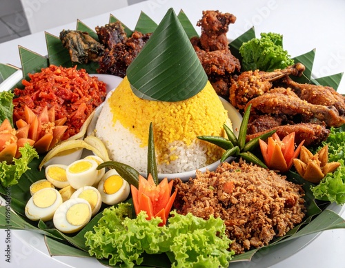 Traditional Indonesian Rice Tumpeng with many topping like egg, vegetables, tempeh, chicken, chili, sambal, cucumber, noddle, yellow rice and make mountain shape in the middle with banana leaf as base