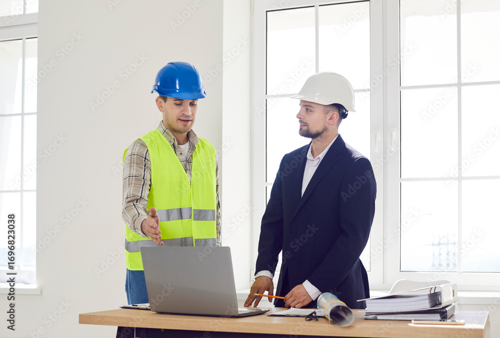 Foreman discussing with young man architect design project or repair of new apartment on a laptop standing in empty white room. Meeting with builder about interior decoration. Moving concept. Foreman discussing with young man architect design project or repair of new apartment on a laptop standing in empty white room. Meeting with builder about interior decoration. Moving concept.