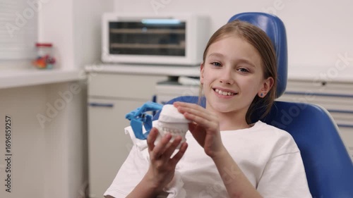 Dental clinic, Dental health, Dental treatment. Young girl examines model teeth while seated in dental chair in modern clinic.