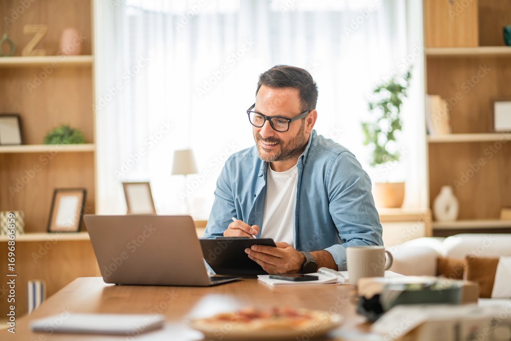 Obraz premium Smiling freelancer working from home taking notes on clipboard