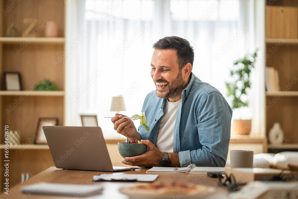 Obraz premium Happy entrepreneur enjoying healthy lunch while working remotely from home office