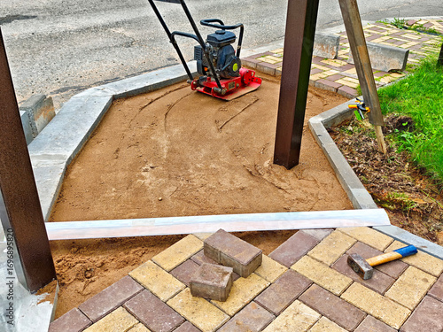 Construction of a patio base with compacted sand and paving bricks in a residential area during daylight
