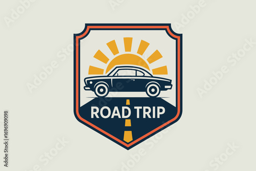 A road trip badge with a car and sun rays in a shield shaped frame with the words road trip below car